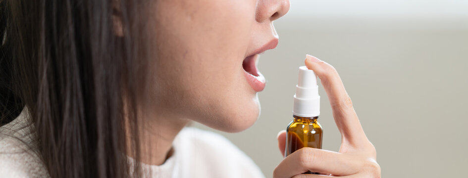 Woman spraying medication into her mouth for sore throat or fresh breath.