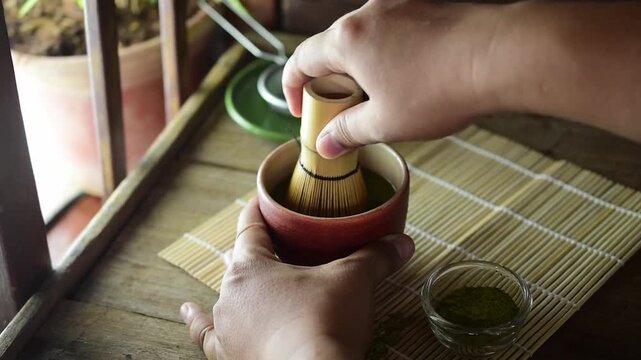 Close up of hand using bamboo chasen whisk to mix green tea matcha powder in a ceramic bowl, traditional Japanese beverage ceremony and healthy wellness concept.