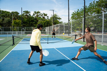 Pickleball player enjoy doubles match on outdoor court, standing ready to hit ball with paddle over net during competitive team sport recreation game workout © winnievinzence