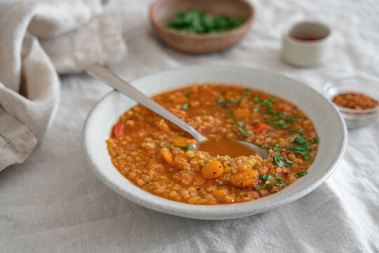 Hearty lentil soup served in a rustic bowl on a natural linen tablecloth. High protein comfort food concept featuring fiber-rich legumes, wholesome ingredients and nourishing homemade meal