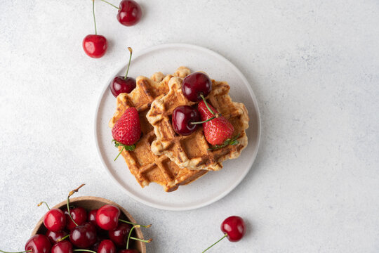 Fresh Belgian cottage cheese waffles served with strawberries and sweet cherries on a light table, top view. High protein breakfast or brunch concept featuring homemade waffles,