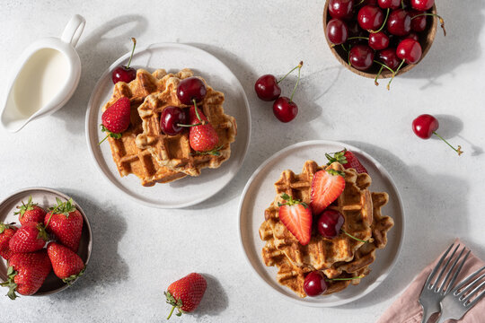 Fresh Belgian cottage cheese waffles served with strawberries and sweet cherries on a light table, top view