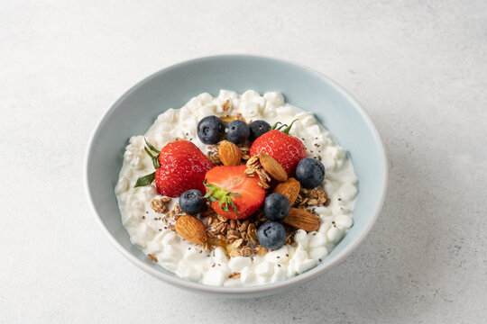 Fresh high protein cottage cheese berry bowl with blueberries, strawberries, chia seeds, granola and almonds served on light background with copy space