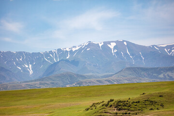 Fototapeta premium Vast green plains stretch beneath snow-dusted mountain peaks