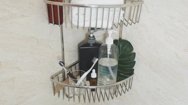 Reducing visual clutter. Modern bathroom shower caddy holding various personal care products, hygiene items, and clean towels against a marble wall
