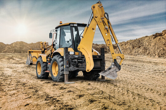 A universal excavator loader is moving dirt at a construction site as the sun shines. Mounds of earth are visible all around the machinery