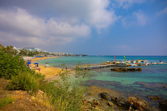 View on Protaras (Paralimni) sand beach with hotels, promenade, tourists, umbrellas, sunbeds near Mediterranean seashore, Cyprus
