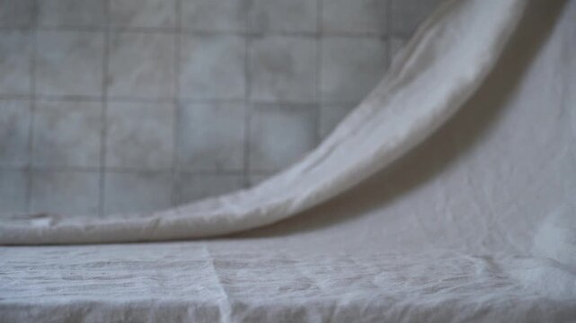 Slow motion video of a table being gently covered with a natural linen tablecloth. Minimalist home styling concept featuring soft fabric movement, warm natural textures and calm domestic atmosphere