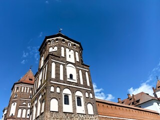 Obraz premium Horizontal low angle wide shot of the majestic Mir Castle complex brick towers and defensive walls under a blue sky, Belarus
