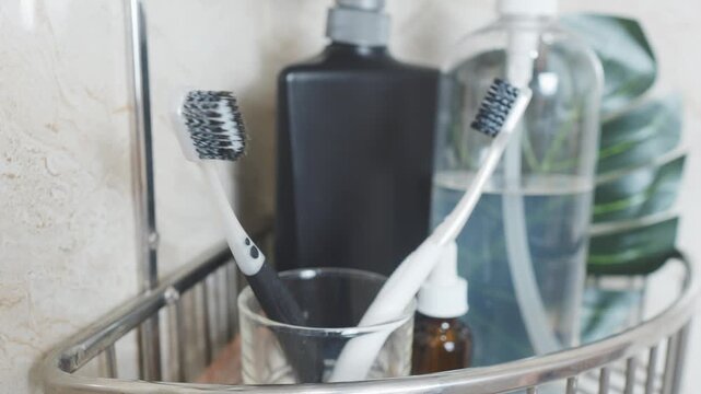 Reducing visual clutter. Two toothbrushes standing in a glass cup on a metal shower caddy shelf, surrounded by various bottles for personal care