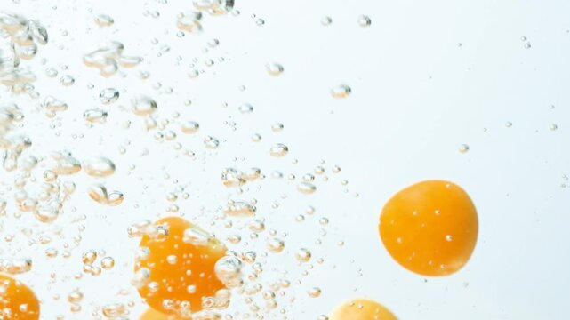 Slow motion shot of physalis fruits submerging into clean water with air bubbles.