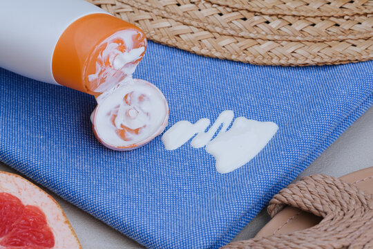 Close-up of white sunscreen lotion spilled onto blue fabric with summer accessories nearby. Concept cosmetic stains on the cloth. top view