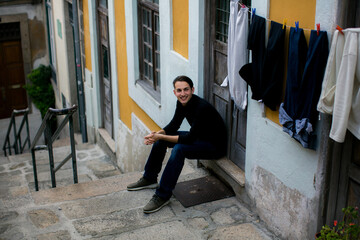 Young man sitting in a traditional Porto street beside colorful houses and hanging laundry capturing everyday urban life in Portugal © De Visu