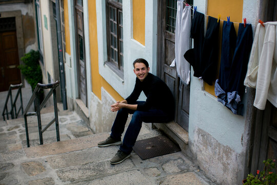 Young man sitting in a traditional Porto street beside colorful houses and hanging laundry capturing everyday urban life in Portugal