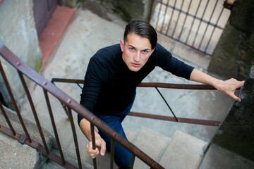 Young man climbing an outdoor stone staircase looking up toward the camera creating a dynamic urban portrait with strong perspective © De Visu
