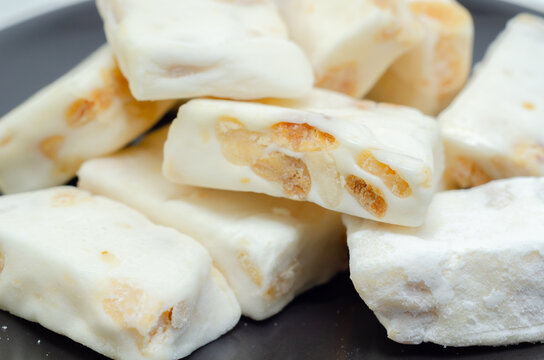 White nougat bars with nut pieces rest on a dark plate