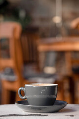 Obraz premium Cup of cappuccino on a weathered white wooden stool in a cozy café interior. Warm natural light, shallow depth of field, visible film grain and analog-inspired aesthetic create a calm.