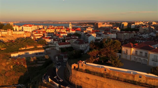 The drone passes over the orange clifftop settlement where historic buildings sit at the edge of dramatic rocky walls.