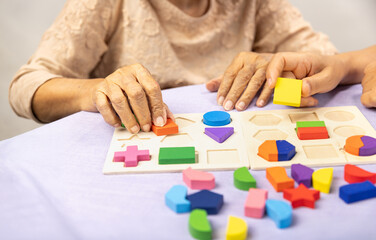 Fototapeta premium Caregiver and senior woman playing wooden shape puzzles game for dementia prevention.