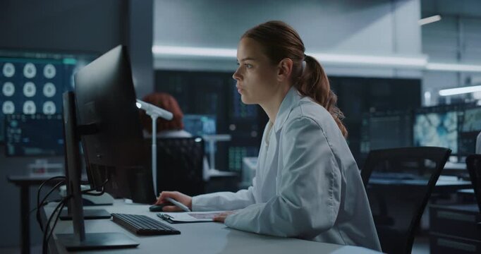 Portrait of a Focused Young Caucasian Female Scientist Working on a Computer in a Modern Medical Research Laboratory, Analyzing Brain Scan Data for Drug Development and Disease Treatment.