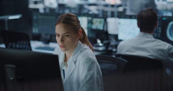 Portrait of Female Scientist Works Intently on a Computer in a High-tech Medical Research Facility While a Male Colleague Studies Brain Scan Data Nearby, Leveraging Ai Technology for Drug Development.
