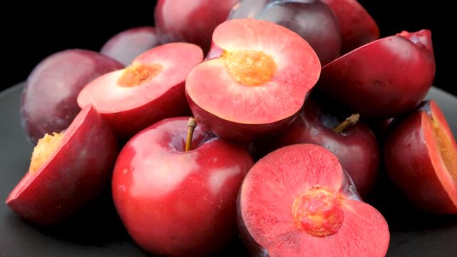 Rotating of halved ripe plums showing juicy red flesh