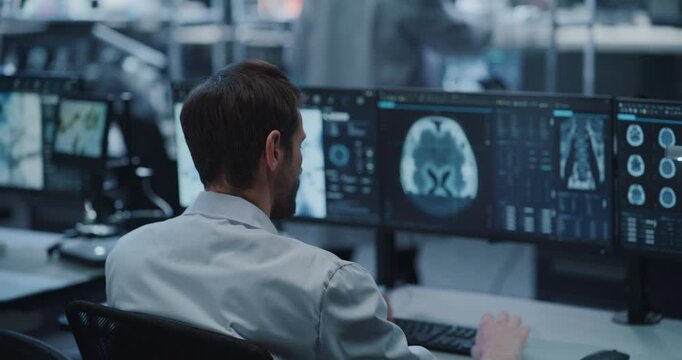 Side Portrait of Male Scientist Reviews Neurological Brain Scan Imagery Displayed on Screen at His Desk in Advanced Medical Research Laboratory, Leveraging AI for Drug Development