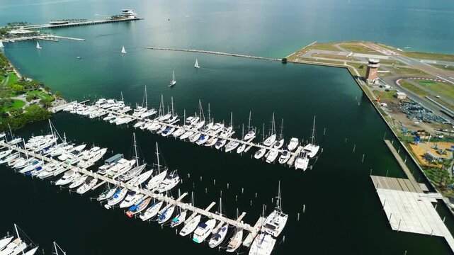 A drone orbits over a marina crowded with rows of docked yachts along the coast.