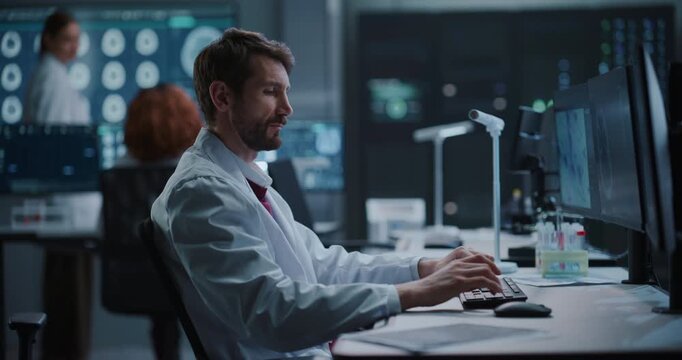 Portrait of Male Scientist Types on a Keyboard While Examining Neurological Brain Scan Data Shown on Monitors in  Medical Research Laboratory, Applying AI for Drug Development and Disease Treatment.