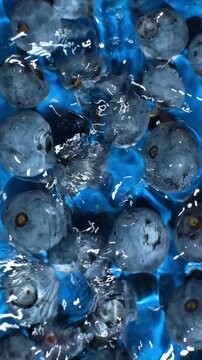 Slow motion top view of blueberries in splashing blue water.
