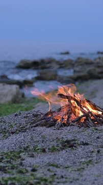 Bonfire burning on a rocky beach at dusk with sound of ocean waves