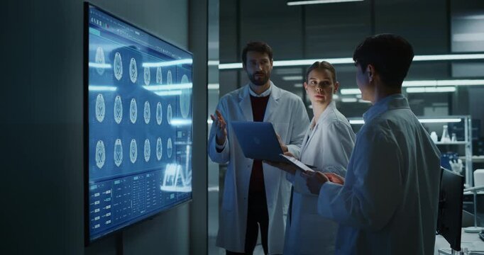Multiethnic Scientists Meeting and Talking, Examining MRI Brain Scans on a Big Screen With Laptop in a High-tech Hospital Lab, Advancing Neurology Drug Research and Disease Treatment Therapy.