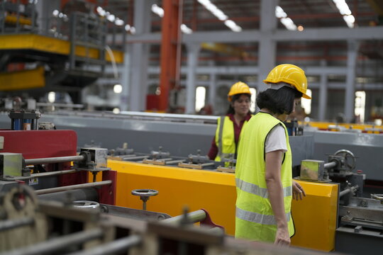Workers are in a factory setting, carrying out tasks with machinery and tools during daytime