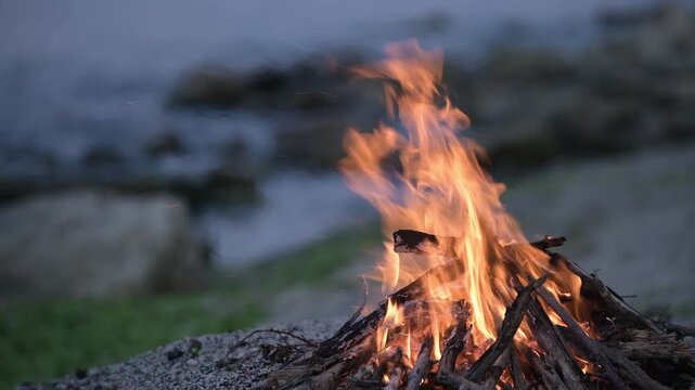 Bonfire burning on a rocky beach at dusk with sound of ocean waves
