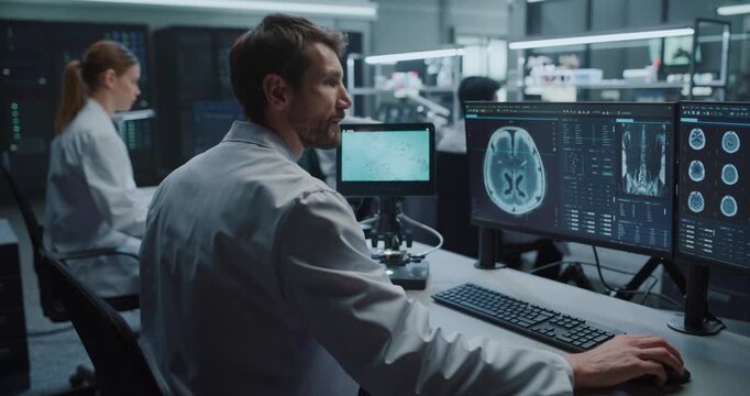 Male Scientist Operates Digital Microscope to Study Specimens While Reviewing MRI Brain Scans on Monitors in Hospital Laboratory, Team Researches Pharmaceutical Drugs for Neurological Disease
