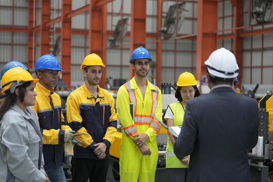 Workers listen to a safety briefing led by a supervisor in a factory setting during daytime hours