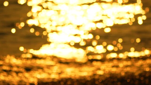 Golden sunset ocean waves glisten as tides roll against the rocky shore during dusk. Extreme close-up soft focus shot.