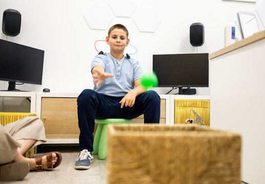 A child between 10 and 12 years old performs a play audiometry with headphones during a pediatric ear, nose, and throat hearing evaluation with a ball.