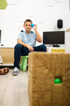 Vertical photo of a child between 10 and 12 years old performing a play audiometry with headphones during a pediatric ear, nose, and throat hearing evaluation with a ball.