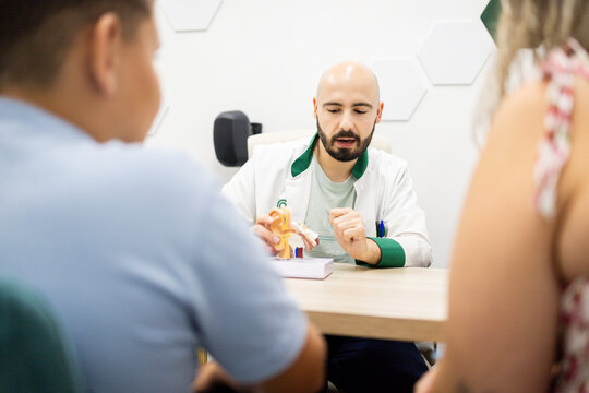 ENT doctor explaining ear anatomy model to couple during medical consultation in clinic.Concept of otolaryngologist.