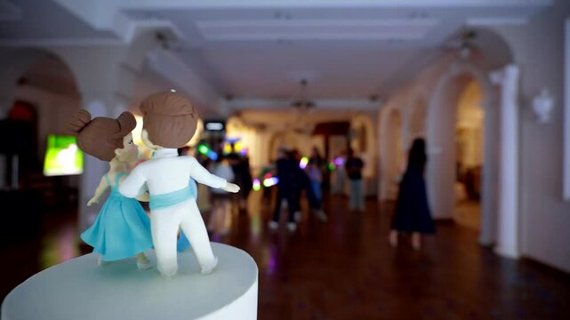 Close-up of a wedding cake topper dancing figurines with blurred people dancing in the background during a banquet. copy space