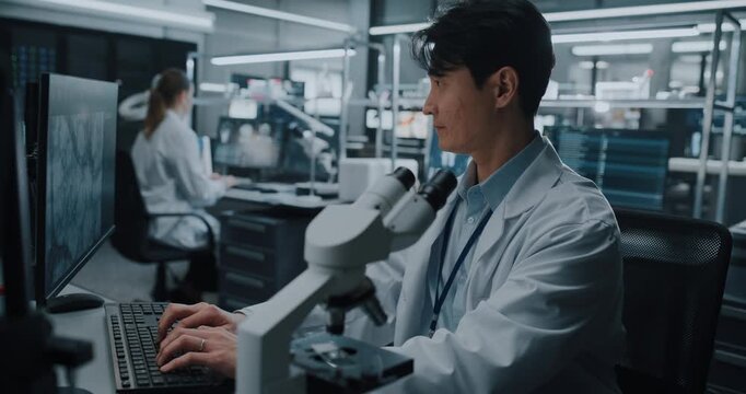 Portrait of Asian Male Scientist Looking Under Microscope, Inspecting Biological Samples While Typing Findings. Team of Researcher Work on Drug Development in Advanced Medical Hospital Laboratory