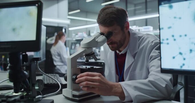 Portrait of Male Scientist Lookung Under Microscope Inspecting Specimen Slides. Researcher Analyzes Molecular Data in Medical Hospital Laboratory Pharmaceutical Drug Discovery. Zoom out Cinematic Shot