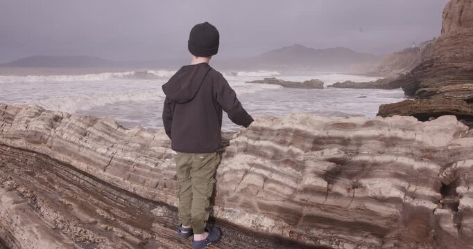Young Boy in Hoodie Watching Ocean Waves at Spyglass Park, Pismo Beach, California