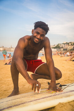 Young man waxing surfboard anticipating summer surf session