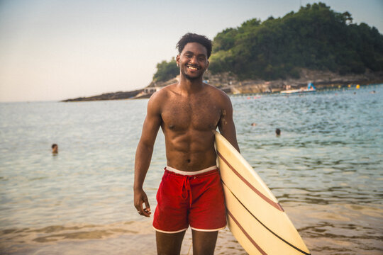 Young smiling man holding a surfboard on beach