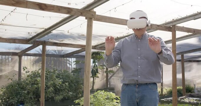 Mid adult man wearing VR headset receiving cues, making pinch gestures in greenhouse with plants