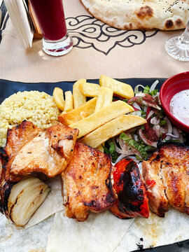 Classic Turkish tavuk sis kebab served with bulgur rice, french fries, grilled vegetables, sumac salad, and pita bread. Commercial food concept.
