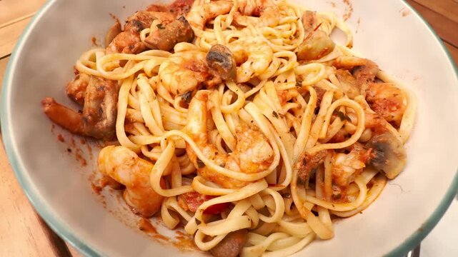 Closeup zoom in shot of a bowl of linguine pasta in sauce, with fried king prawns and mushrooms, on a table ready to eat.