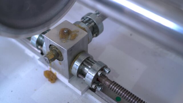 Close-up of industrial machine gearbox and rotating threaded rod in a factory